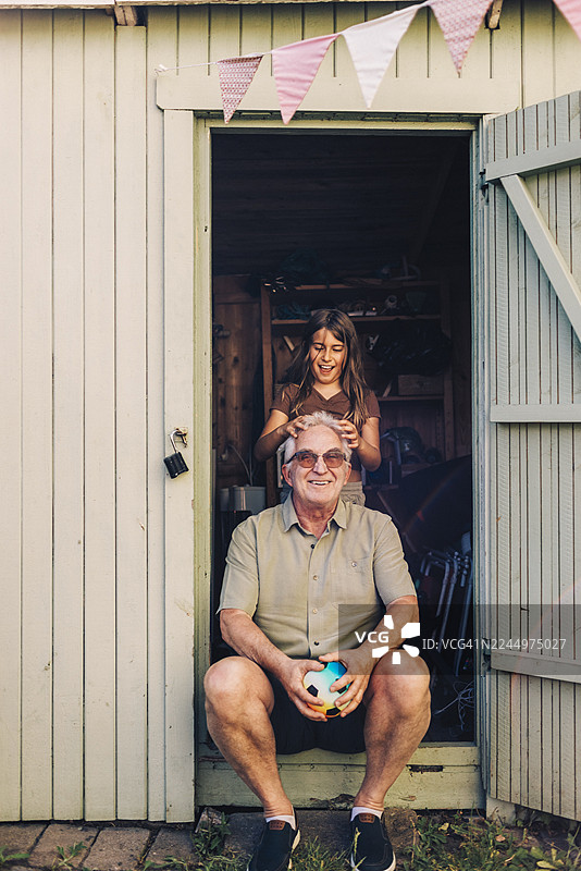 快乐的女孩在后院的木屋门口为爷爷按摩头部图片素材