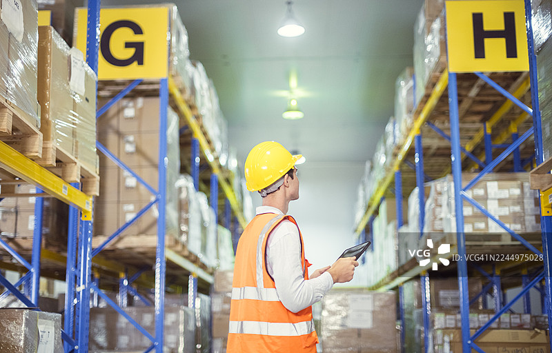 戴着安全帽的仓库工人正在有条理的仓库通道中扫描库存，确保高效的物流和供应链管理。图片素材
