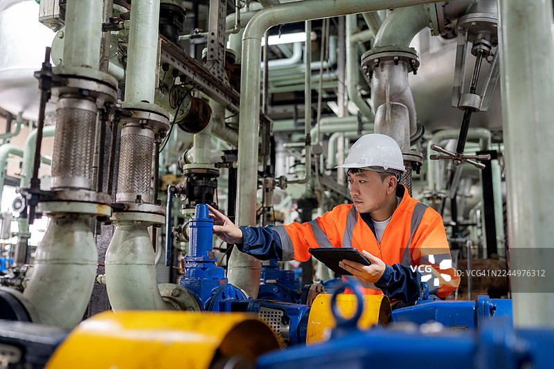 一名维修工程师在润滑油工厂内，使用数字平板电脑通过在线监控系统检查泵的性能。预防性维护确保了工业石油制造运营的安全、高效和可靠。图片素材