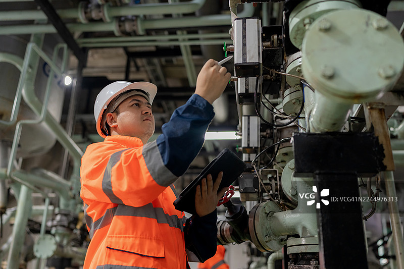 身着安全装备的维护工程师在炼油厂内通过平板电脑检查阀门操作。重点关注石化和能源制造行业的科技、安全和预防性维护。图片素材