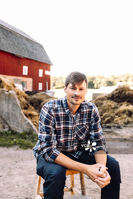 坐在谷仓前凳子上的微笑的牛场工人肖像图片素材