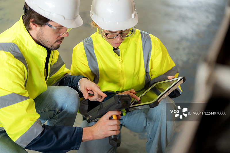 两位仓库员工在宽敞的仓库内使用条形码扫描仪和数字平板电脑检查货物。他们利用现代技术确保物流、货运和全球商业运营的质量控制、安全和效率。图片素材