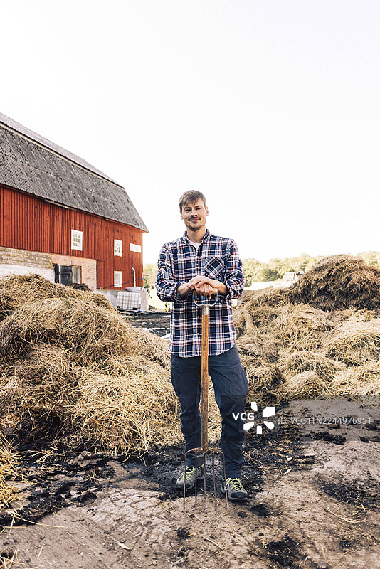 自信的男性农民肖像，手持干草叉，在谷仓前摆姿势图片素材