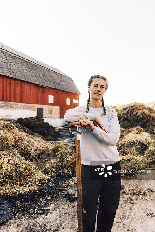 自信的女农夫肖像，倚靠在干草堆旁的谷仓旁，手持干草叉图片素材