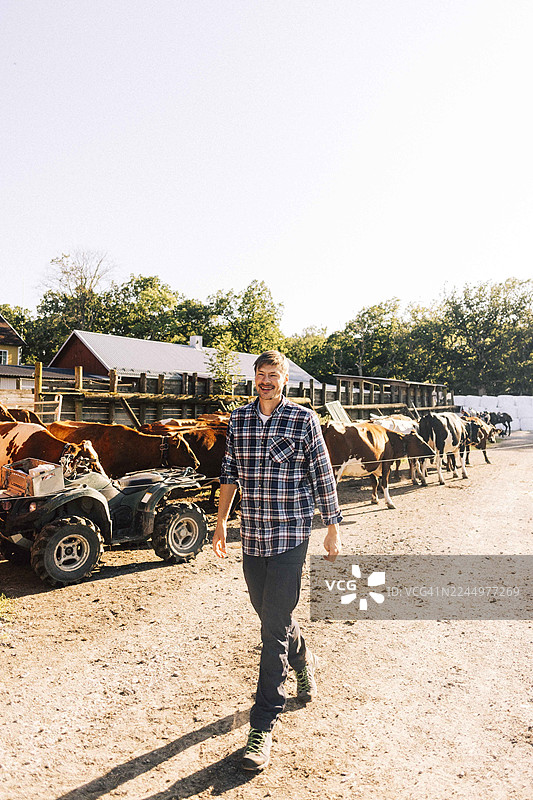 阳光明媚的白天，一位面带微笑的男农民在农田中行走，背景是天空图片素材