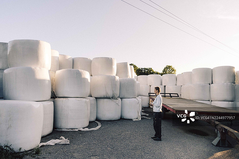 一名农民在农场工作，正在清点堆叠的干草捆，这是他的全身照图片素材