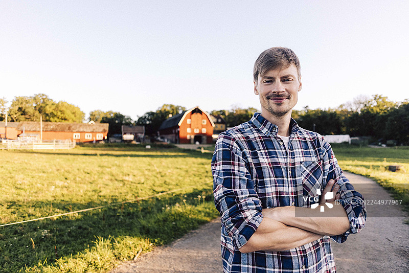 微笑的男性农民，双臂交叉，站在农场的小径上图片素材