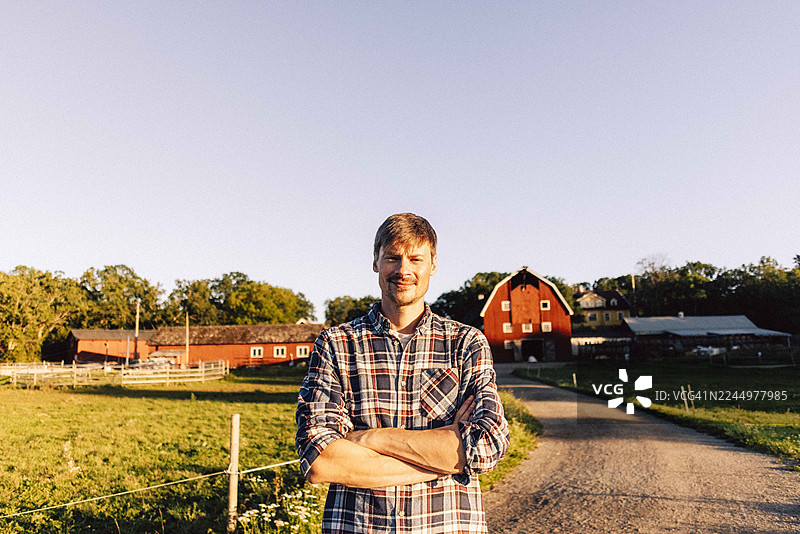 日落时分，自信的农场工人在小路上双臂交叉站立的肖像图片素材