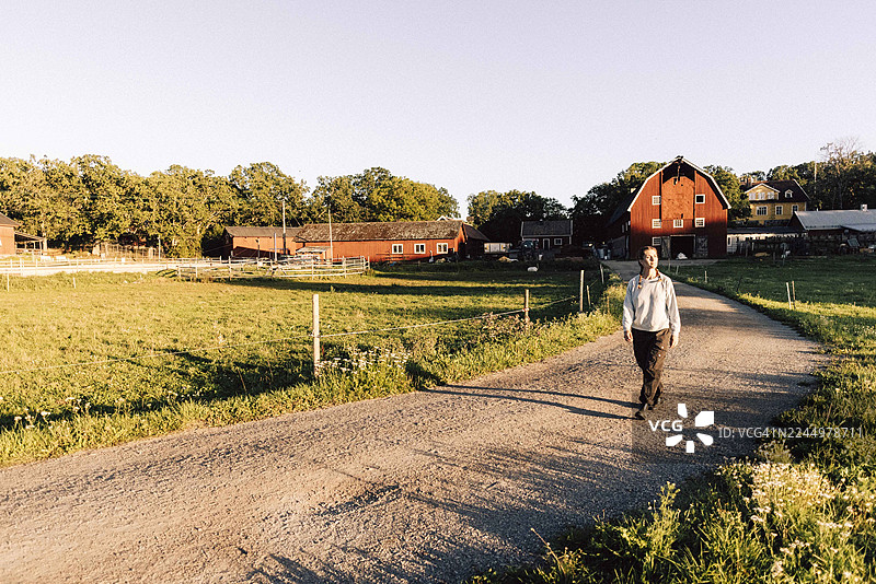 一位女农夫在背景有农场的土路上行走的全景图图片素材