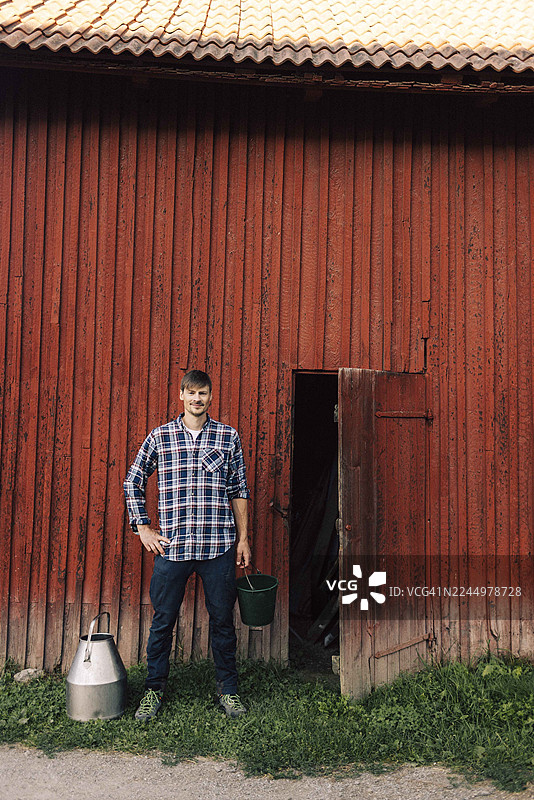 一位自信的男农民，手拿水桶，叉着腰站在谷仓外图片素材