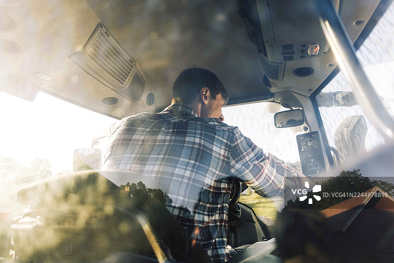 透过玻璃看到的农田里，一位男农民驾驶拖拉机的背影图片素材