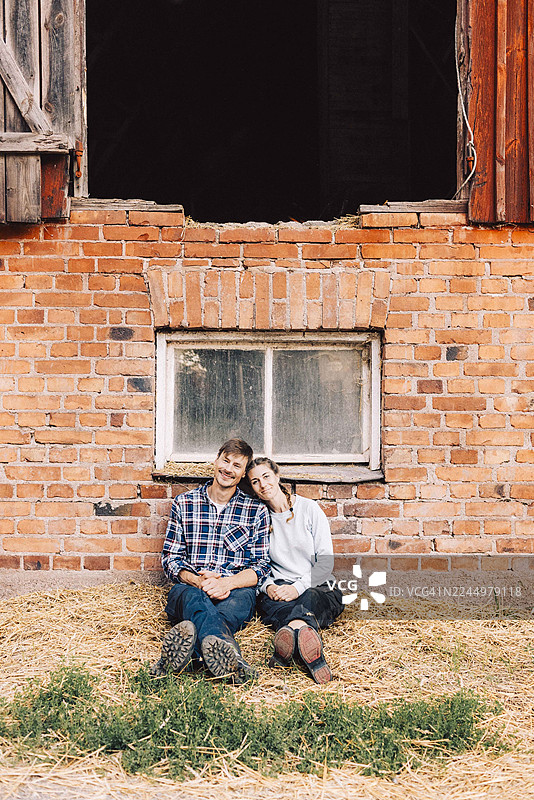 一对幸福的夫妇坐在农场外的砖墙旁，面带微笑图片素材