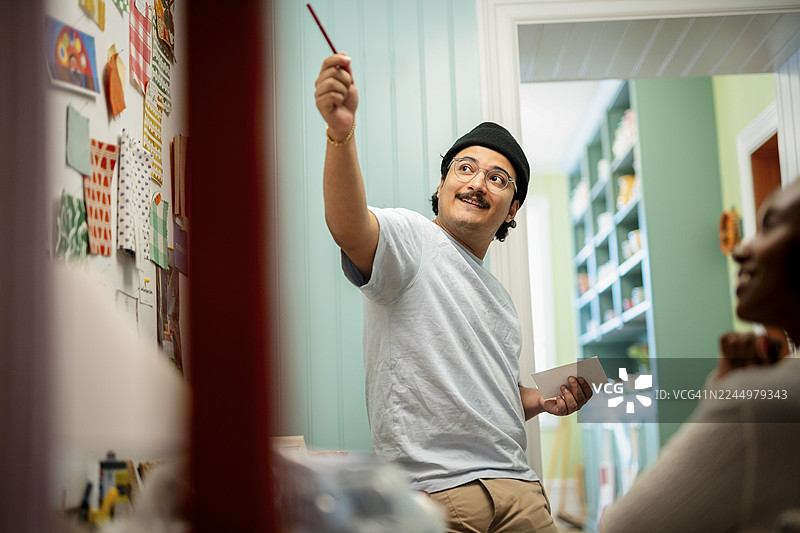 微笑的销售人员手持钢笔并指向，同时在店内与店主交谈图片素材