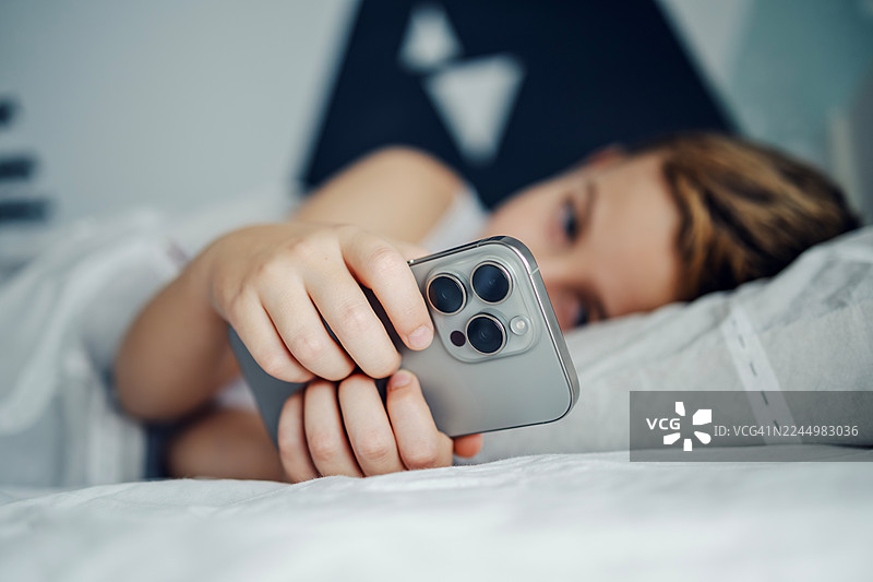 孩子在床上使用智能手机，屏幕时间成瘾概念图片素材