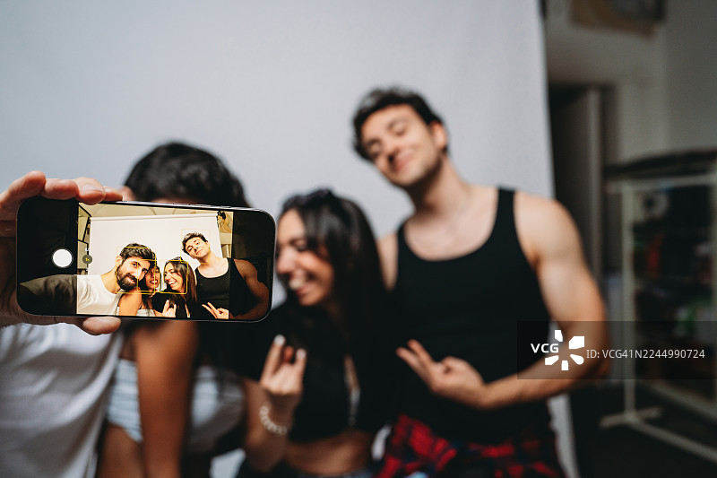 年轻的朋友们在家中聚会时用智能手机自拍图片素材