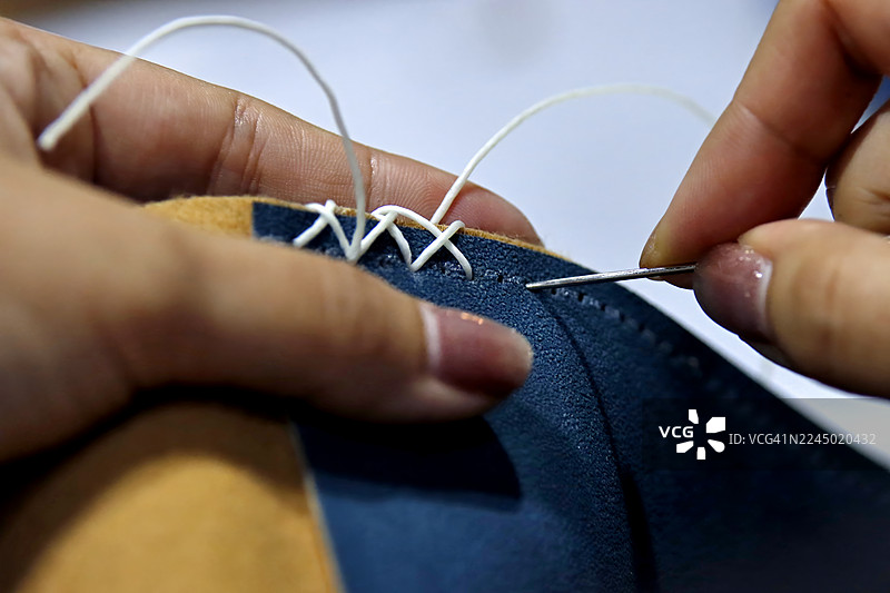 手工缝制皮革制品的精细过程，突出十字绣图案和针法。图片素材