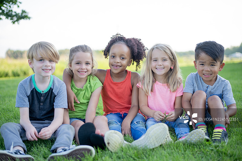 一群快乐的多元化孩子坐在公园的草地上，户外；朋友们在一起大笑图片素材