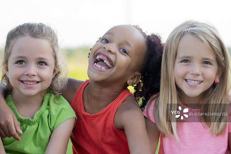 快乐的混血朋友在明媚的阳光下户外欢笑，记录家庭和学校活动的珍贵回忆图片素材