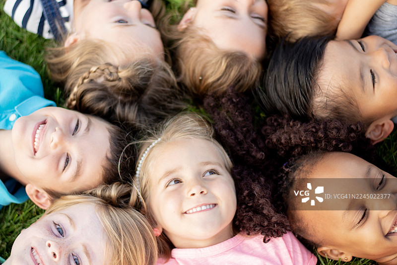 一群快乐的、多元化的孩子们在草地上围成一圈躺着，在户外微笑着大笑图片素材