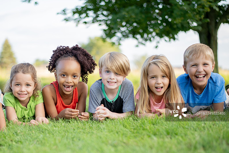 一群快乐的、肤色各异的孩子们躺在户外的绿草地上，分享着欢笑和友谊图片素材