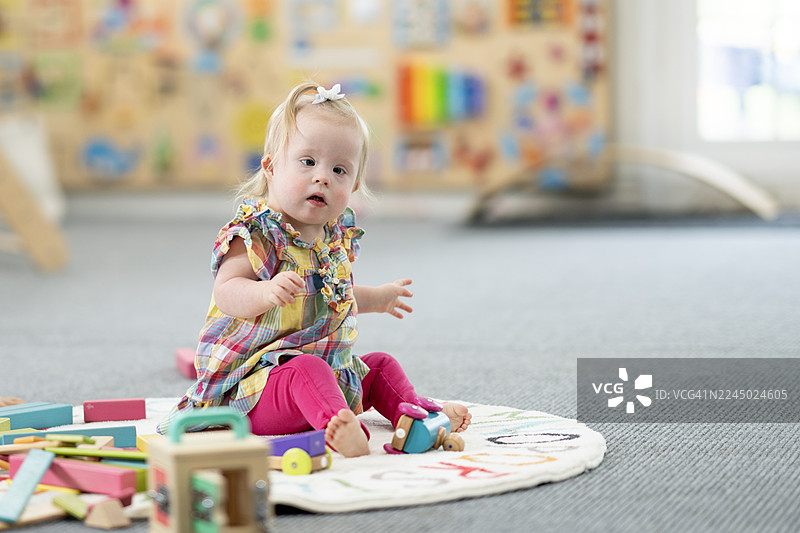 可爱的小女孩在日托中心的垫子上玩着色彩鲜艳的玩具图片素材