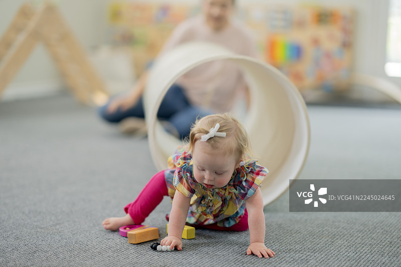 可爱婴儿在室内日托玩耍时间爬行，周围有隧道、积木和彩色玩具图片素材