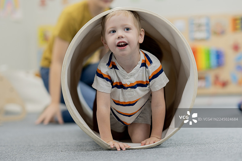 幼儿在日托中心爬行穿过游戏隧道，看护者在附近图片素材