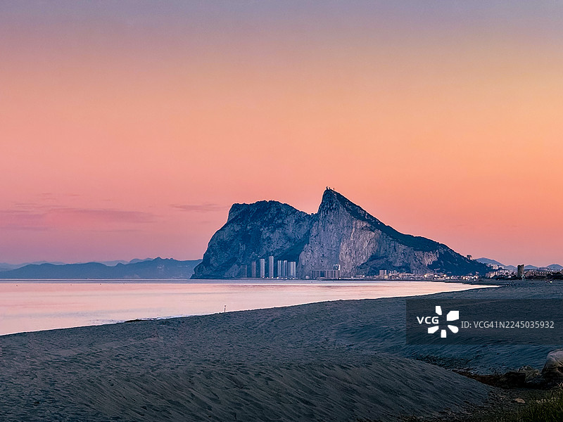 西班牙阿尔卡德萨海滩，日落时分，海景与生动的夜空交相辉映，有醒目的岩层和远处的城市灯光图片素材