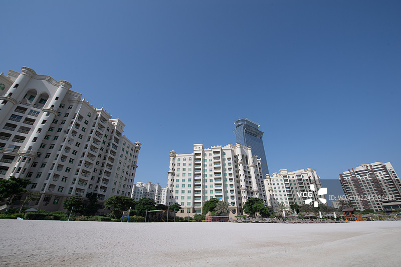 从沙滩仰望迪拜现代建筑和摩天大楼，背景是蔚蓝无云的天空图片素材