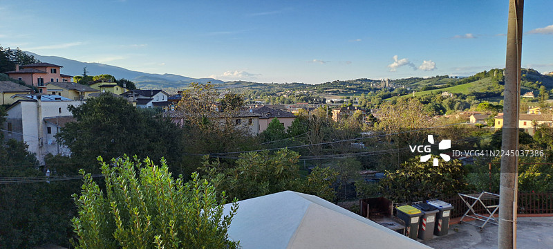 从高处俯瞰，风景如画的小镇坐落在山谷中，周围是连绵起伏的丘陵，天空湛蓝，意大利，斯波莱托，圣乔瓦尼迪拜亚诺图片素材