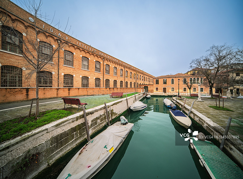 船只停泊在威尼斯的一条运河中，周围环绕着历史悠久的砖砌建筑，天空晴朗，意大利威尼斯图片素材