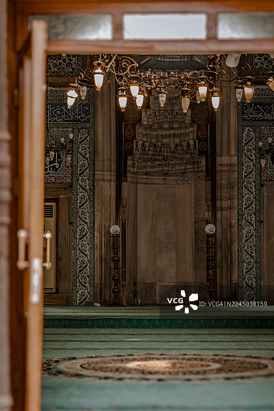 透过一扇敞开的木门，可以看到传统清真寺华丽的室内，包括米哈拉布、吊灯和图案地毯。图片素材