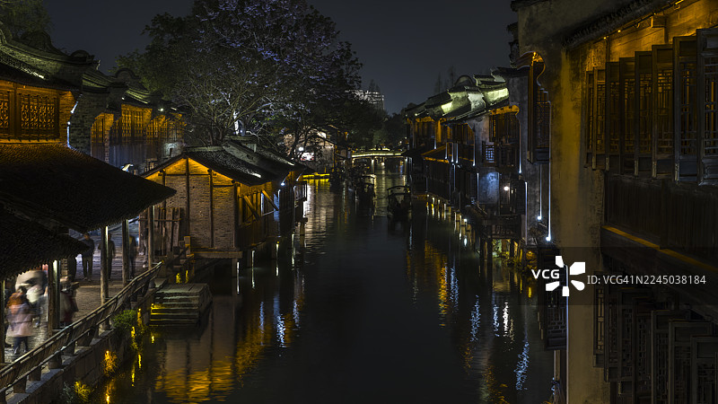 中国乌镇，运河沿岸历史建筑的夜景，模糊的身影沿着灯火通明的路径行走，乌镇，中国图片素材