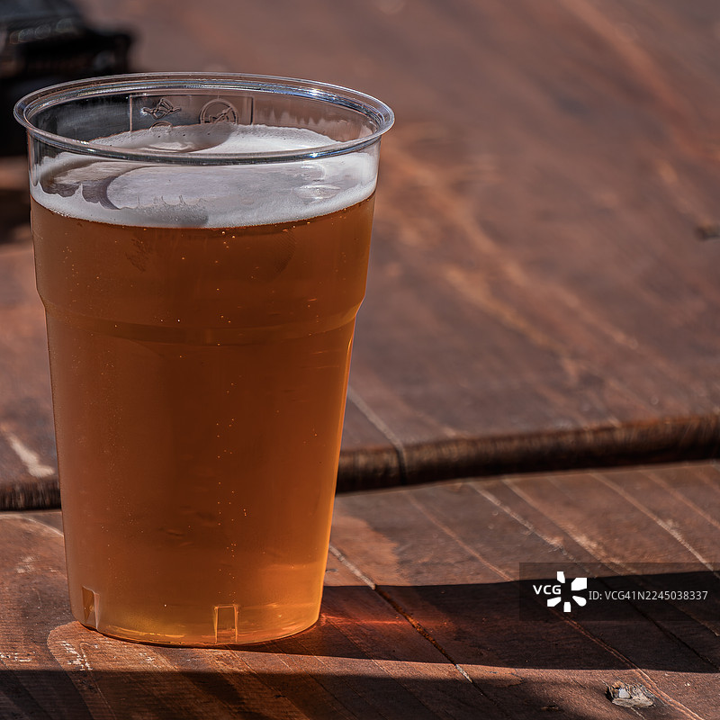 阳光下，木桌上塑料杯中清爽的饮品特写图片素材