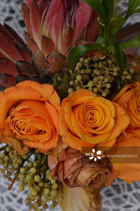 特写镜头，一束色彩鲜艳、种类繁多的花束，包含橙色玫瑰、帝王花以及各种绿色填充植物，非常适合特殊场合或家居装饰图片素材