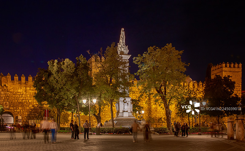 西班牙塞维利亚，圣母无染原罪雕像与阿尔卡萨尔城墙的夜景图片素材