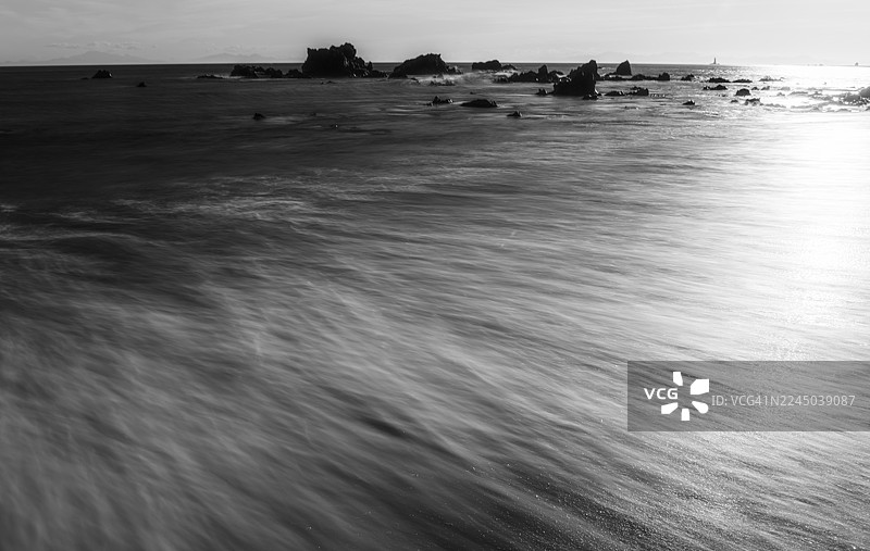 新西兰惠灵顿，明亮天空下的海浪和岩石海岸的长时间曝光黑白照片图片素材