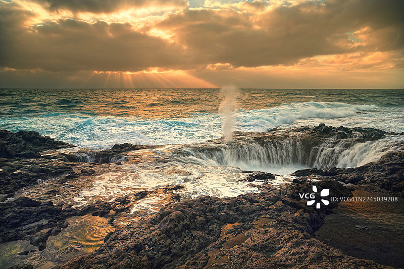 西班牙，戏剧性的日落映照着岩石海岸，海浪拍打着海蚀洞和天然水池图片素材