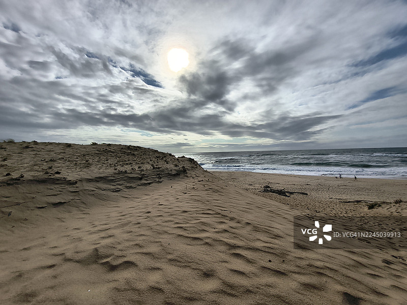 法国兰德省，沙滩上空阴云密布，海浪翻滚，远处有人影绰绰图片素材