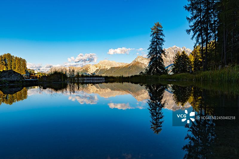 瑞士苏奥尔·弗坦格隆德，夕阳下宁静的山间湖泊倒映着天空与松树图片素材