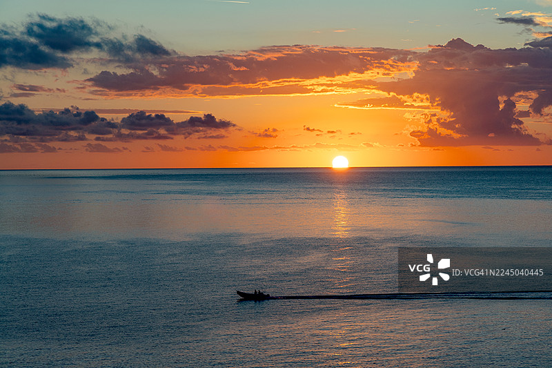 夕阳西下，一艘小船在宁静的海洋上缓缓驶过，余晖洒满地平线和云彩，意大利西罗洛图片素材