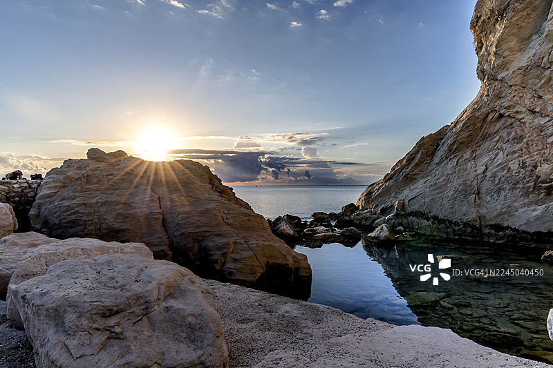 意大利西罗洛，戏剧性的日落映照在崎岖的海岸线上，阳光穿透天空，倒映在平静的海面上图片素材