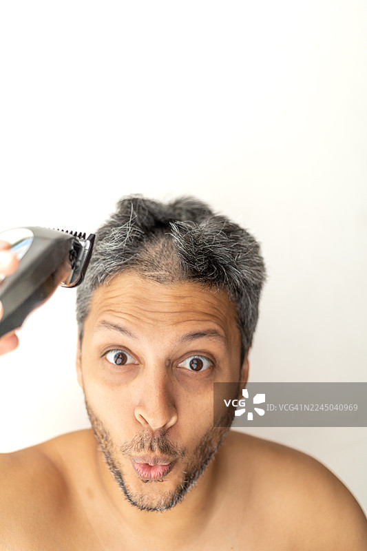 一名男子表情惊讶地用电动剃须刀剃光头，背景为白色图片素材