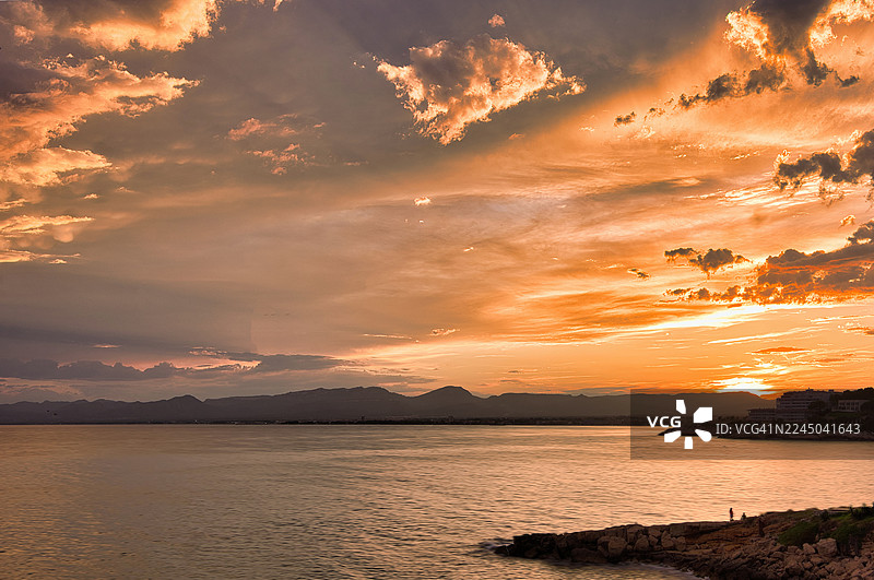 西班牙萨洛卡普萨洛，岩石海岸边宁静大海上的壮丽日落，远处的山脉图片素材