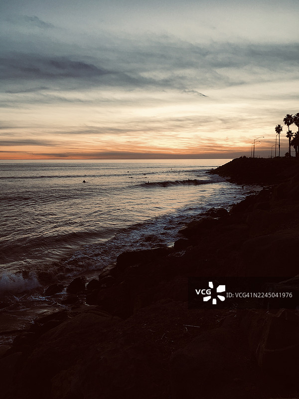 日落时分，海面宁静，天空戏剧性地变幻，水中还有冲浪者图片素材