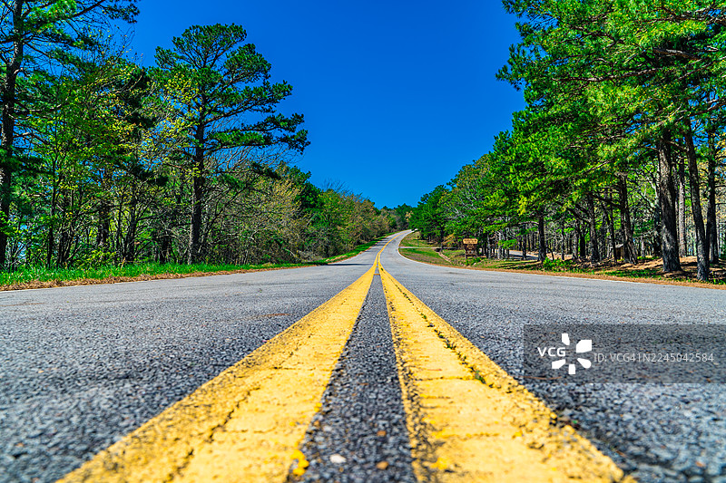碧空如洗，一条蜿蜒的道路穿过郁郁葱葱的绿色森林，召唤着旅行与探险。美国，俄克拉荷马州，塔利海纳，塔利梅纳国家风景道图片素材