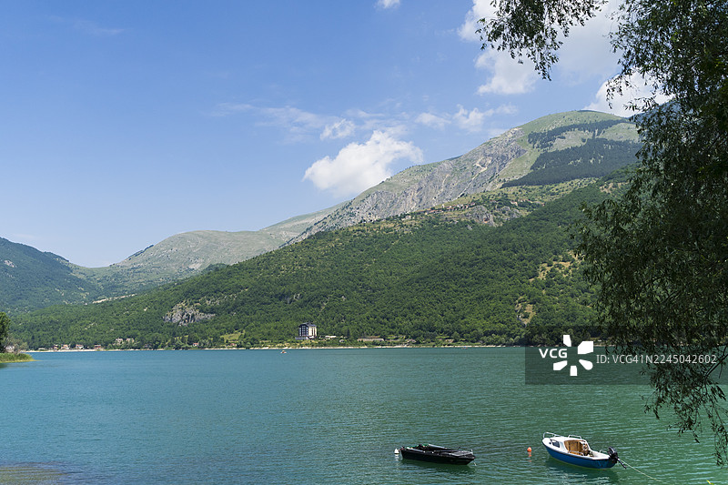 晴朗蓝天下，宁静的湖泊、船只和苍翠的山峦构成了一幅风景画图片素材