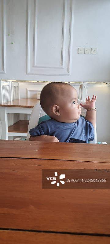 好奇的男婴坐在木制高脚椅的桌子旁，看向别处图片素材