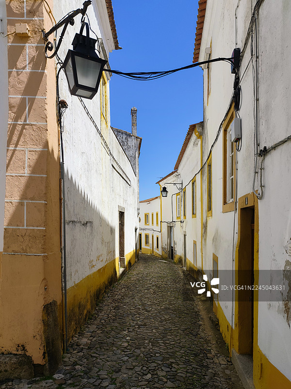 葡萄牙一座欧洲城市，晴朗的蓝天下，鹅卵石铺就的小巷蜿蜒穿过历史建筑图片素材