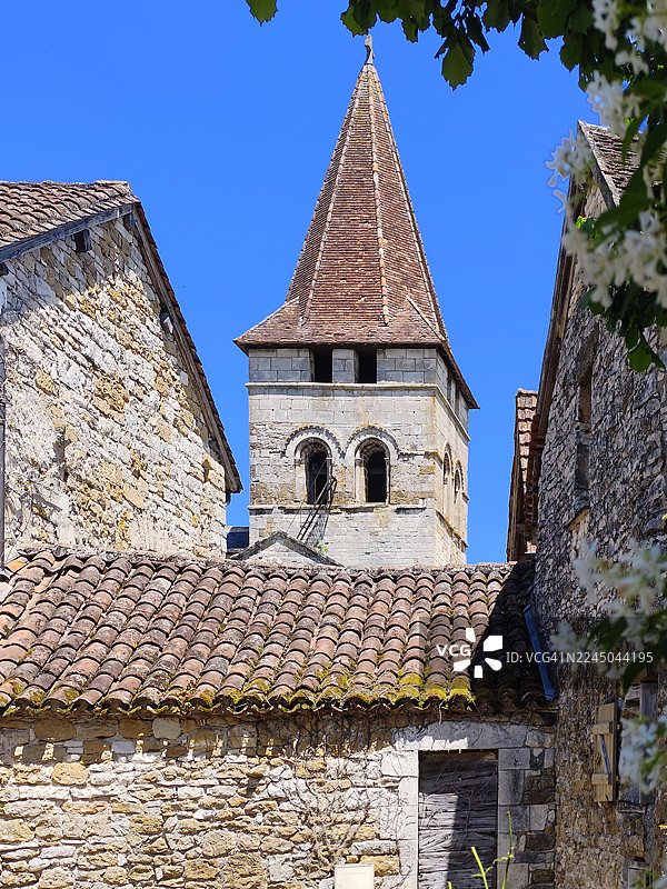 仰视老教堂钟楼，有瓷砖屋顶，背景是晴朗的蓝天，周围是传统的石头建筑，法国戈尔东，卡雷纳克图片素材